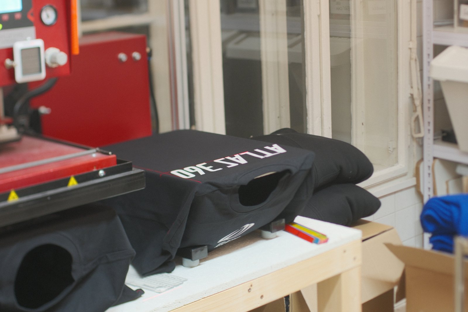 Stapel der schwarzen Atlas-360-Shirts und -Pullover beim Press-Vorgang — Launch-Auflage für das Hyrox-Gym Graz