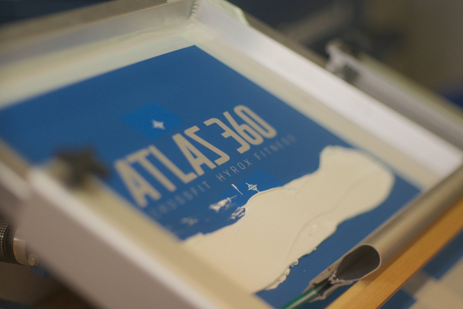 Sieb beim Siebdruck-Vorgang mit weißer Plastisol-Farbe für das Atlas-360-Motiv im klassischen Direkt-Siebdruck
