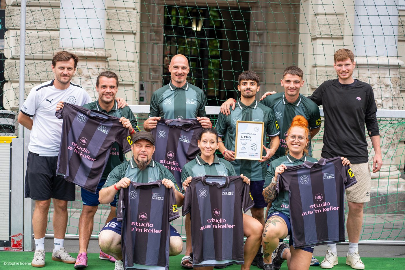 Siegerteam des streetfootbALL Festivals Graz hält die grauen Gewinnertrikots mit „studio aus'm keller