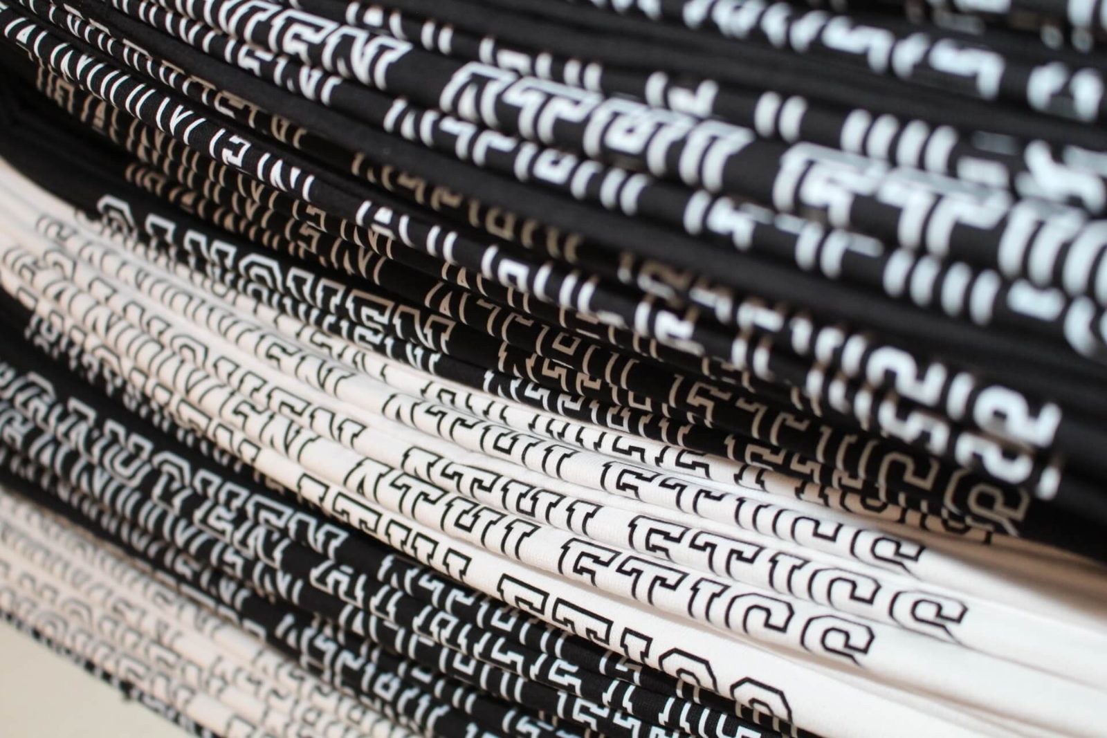 Stapel frisch bedruckter Ganoven-Athletics-Shirts in Schwarz und Weiß, gefaltet nach der Produktion