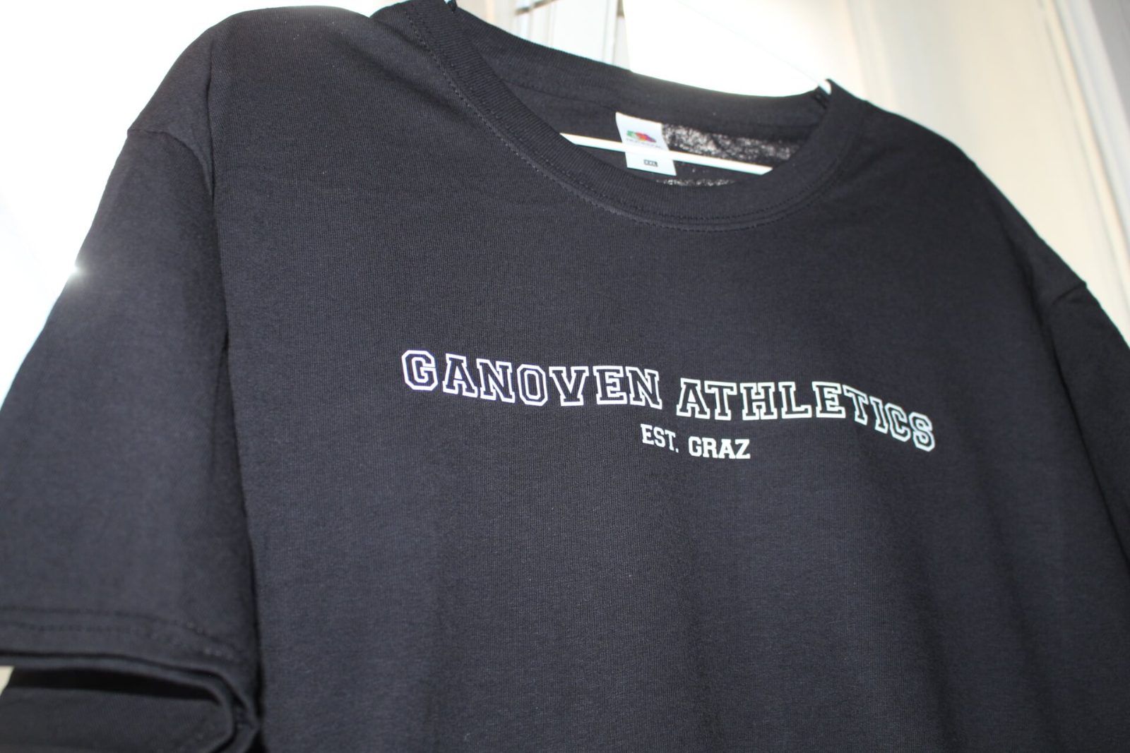 Detail des weißen „Ganoven Athletics Est. Graz“-Siebdrucks im College-Style auf schwarzem T-Shirt