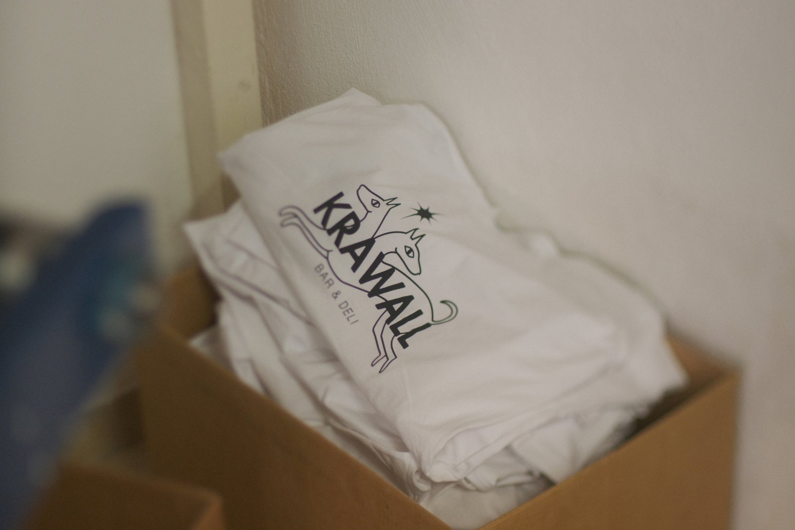 Stapel der Krawall-Bar-&-Deli-Shirts in Naturweiß mit Brand-Logo (Hund-Schriftzug-Kombination) im Siebdruck