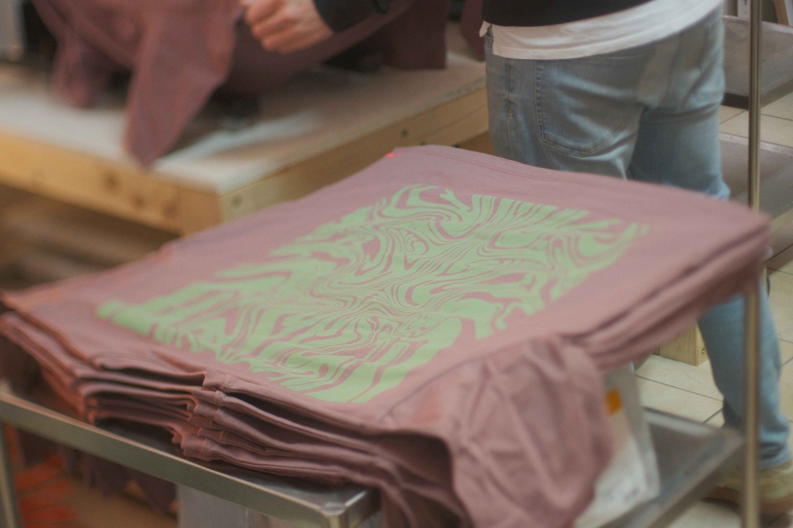 Stapel der fertigen altrosa Maskusi-Ink-Shirts mit mintgrünem Discharge-Swirl-Print