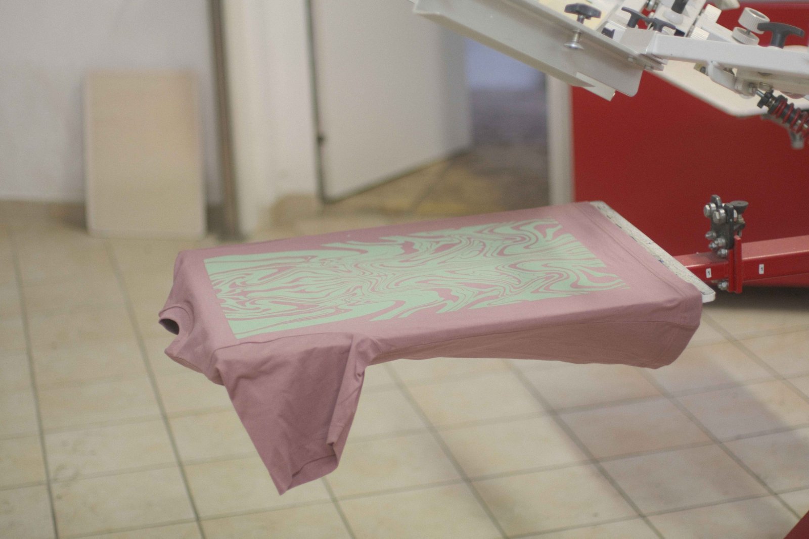 Altrosa Shirt auf dem Druckplaten des Siebdruck-Karussells mit dem fertig geätzten Swirl-Motiv