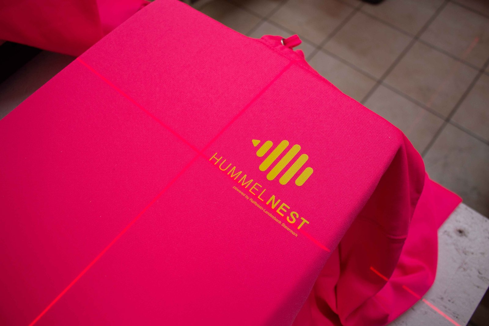 Pinker Hummelnest-Hoodie auf der Press mit Laser-Ausrichtung — Front-Logo im Plastisol-Transfer wird positioniert