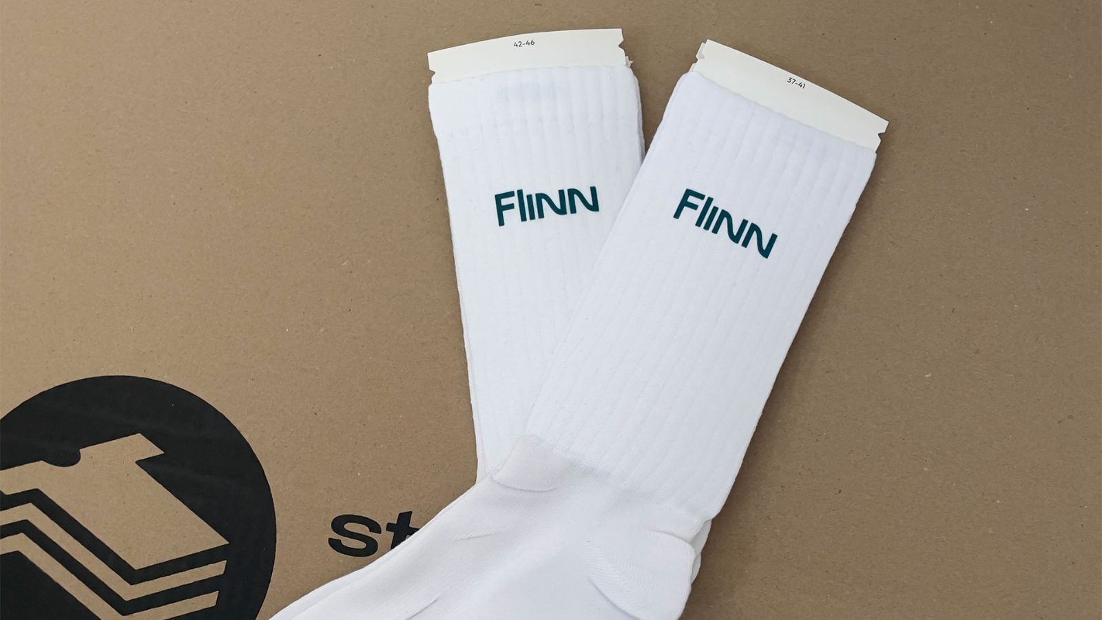 Ein Paar weiße FINN-Socken in den Größen 42–46 und 37–41 auf einer Kartonbox