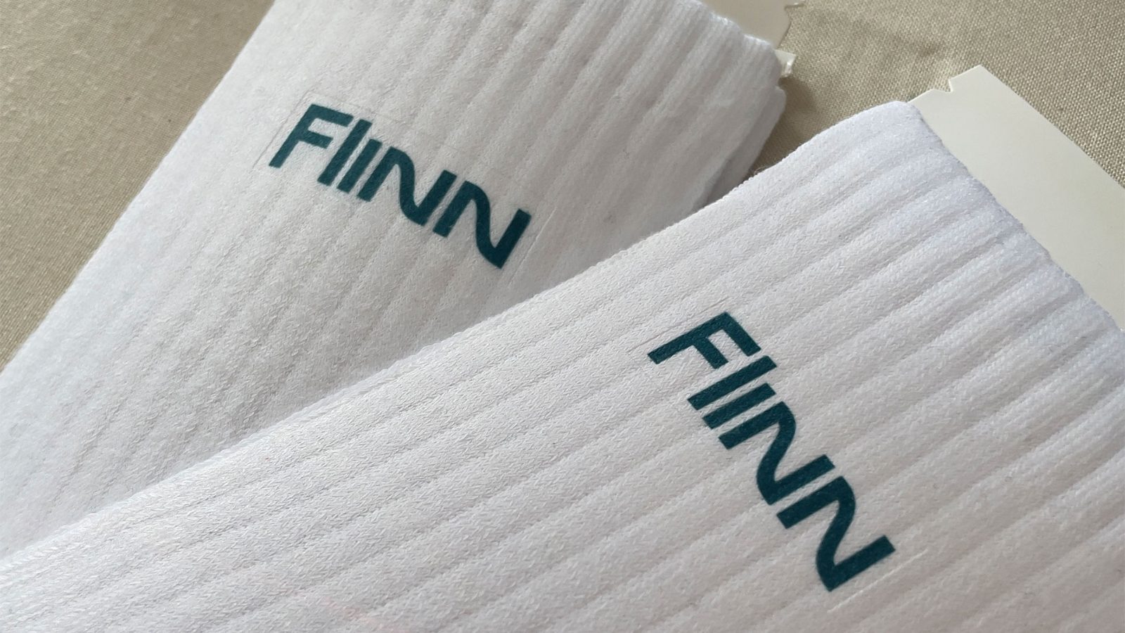 Gefaltete FINN-Socken gestapelt in der Versandbox, alle mit petrolfarbenem Logo und Größe 42–46