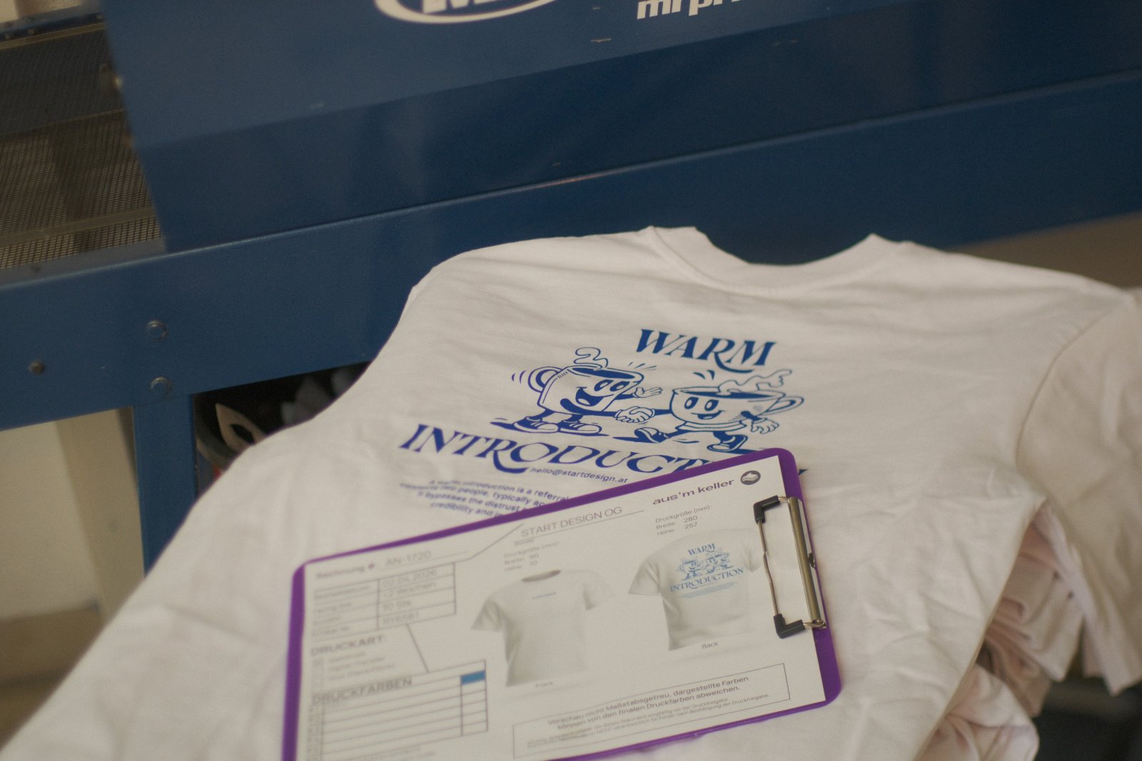 Brand-Shirt der Start Design Agentur mit 'Warm Introduction'-Motiv und zwei Tassen-Maskottchen im wasserbasierten Siebdruck mit Pantone 293 U