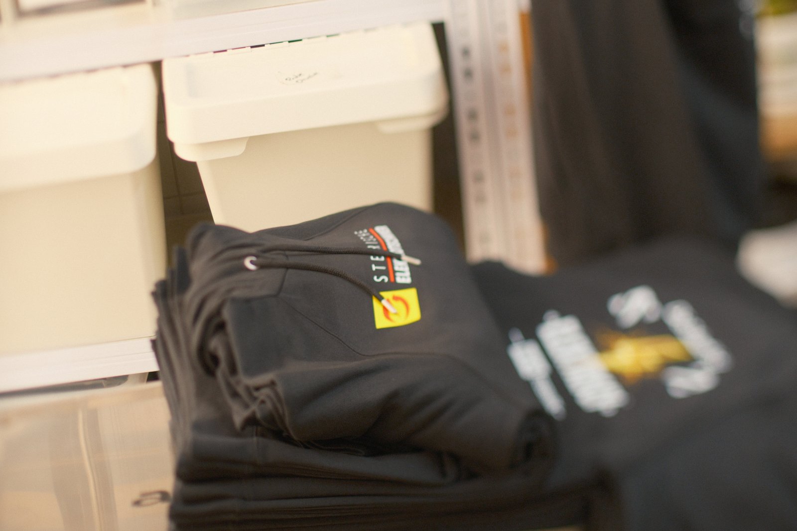 Stapel schwarzer Hoodies der WKO-Steiermark-Kampagne mit Steirische-Elektrotechniker-Wappen am Brust-Patch