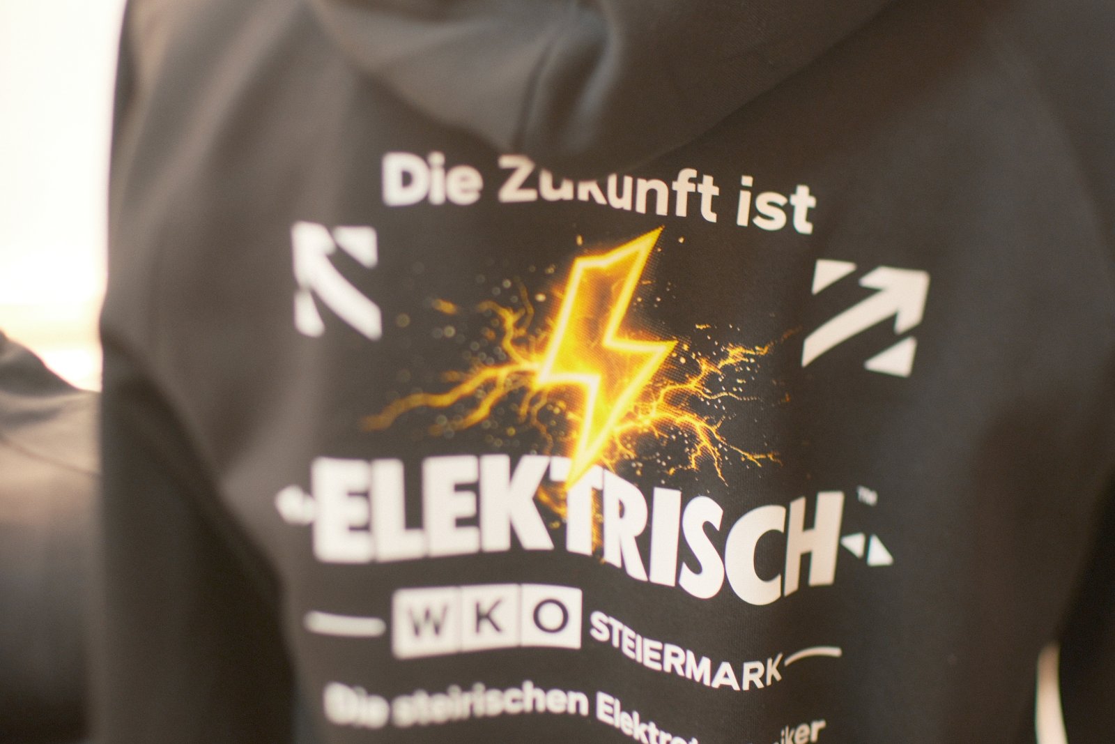 Think-Electric-Tasche mit Blitz-Motiv und Trucker-Cap mit Klett-Patch nebeneinander — Kampagnen-Merch der Steirischen Elektrotechniker