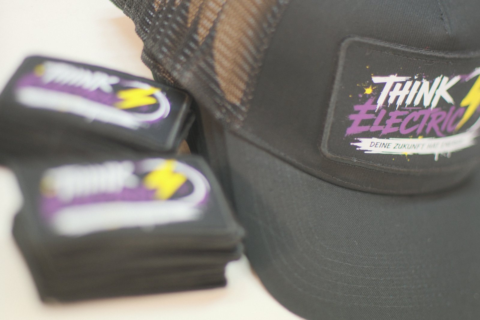 Trucker-Cap mit aufgeklebtem Think-Electric-Patch und Stapel weiterer Klett-Patches daneben zum Austausch